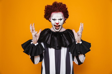 Ugly clown man 20s wearing black costume and halloween makeup looking at camera, isolated over...