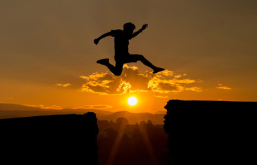 young man jump over the sun and through on the gap of hill silhouette evening colorful sky.image...