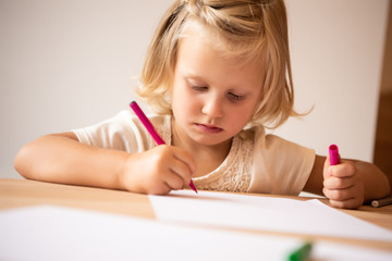 serious adorable kid drawing with pink felt pen in kindergarten