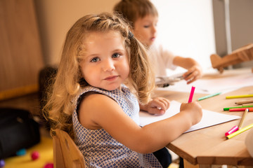 adorable kid drawing in kindergarten and looking at camera