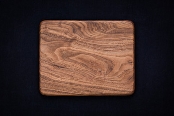 Handmade black walnut rectangular rounded wooden chopping board on black cotton, walnut texture background	
