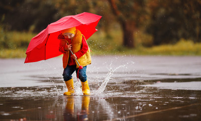 happy child baby boy with rubber boots and umbrella jump in puddle  on autumn walk
