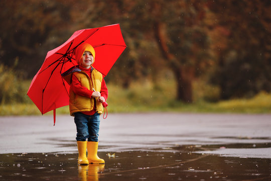 happy child baby boy with rubber boots and umbrella jump in puddle  on autumn walk