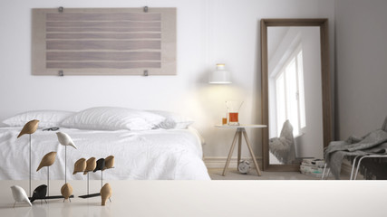 White table top or shelf with minimalistic bird ornament, birdie knick - knack over blurred contemporary bedroom with double bed, modern interior design
