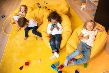 high angle view of multicultural kids lying on bean bag chairs in kindergarten