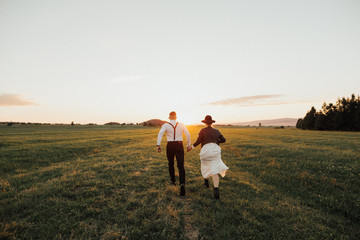 Fototapeta na wymiar Hipster wedding couplekissing on the sunset on green field