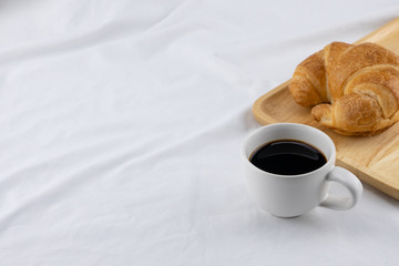 A cup of coffee and croissant on white bed with copy space, selective focus on coffee