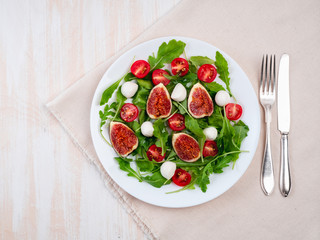 Fresh salad with figs tomatoes cucumbers, arugula, mozzarella. Oil with spices, top view, copy space, white background.