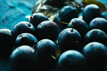 many fresh plums on blue background close up