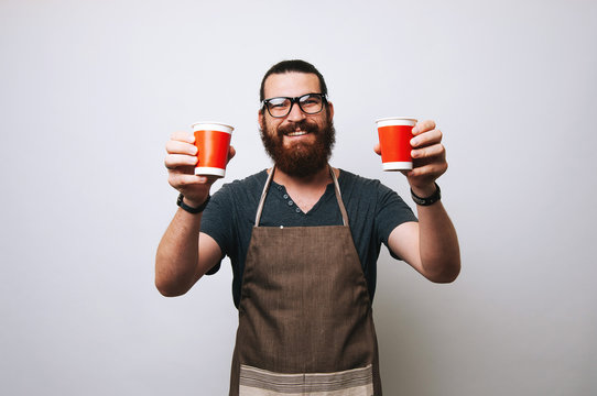 Young Bearded Man Barista Holding Two Cups Of Coffee On The Go .