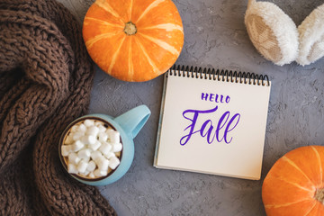 Autumn background with warm knitted scarf, blue mug with coffee, hot chocolate, cocoa, marshmallow, pumpkin, sign Hello Fall, headphones. Concept of warm cozy autumn.