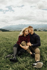 Couple sitting and kissing on grass on the top of mountains enjoying mountains and clouds landscape. Love and travel concept. Lifestyle concept. family active traveling. Mountain view