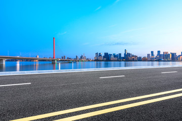 Urban asphalt road and modern buildings with river in Hangzhou at sunrise