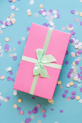 Festive holiday New Year and Christmas blue background with pink gift box, confetti. Concept of carnival, birthday, party. Flat lay. Top view.