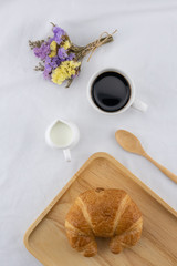 A cup of coffee, milk and croissant with statice flower bouquet on white bed 
