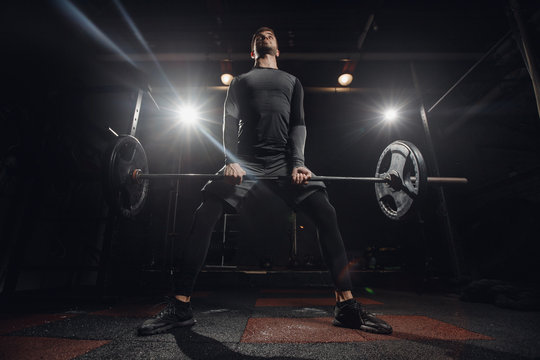 Training with barbell, dark background. Sporty man performs exercise of deadlift.