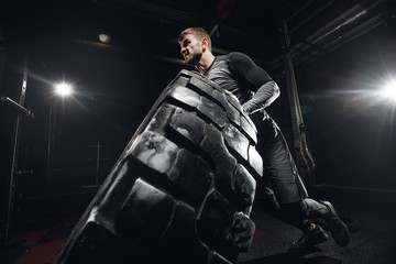 Fototapeta na wymiar Muscular fitness man flipping tire wheel. Concept functional training workout gym