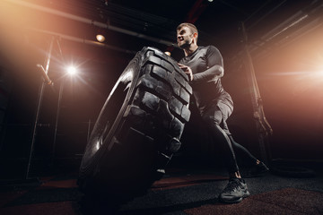 Muscular fitness man moving large tire in gym center, concept lifting, workout training
