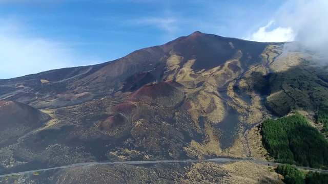 Aerial footage of Mount Etna moving fast towards peak showing coaches driving up the mountain slopes on left side and rough hostile terrain on right edge beautiful steady 4k high resolution quality