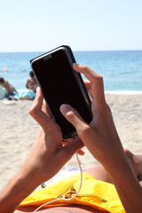 caucasian teenager hand's holding a smartphone lei dow on a sun bed on the beach, clipping path for...