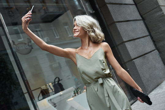 Fashion. Young stylish woman walking on the city street taking selfie photo on smartphone smiling cheerful