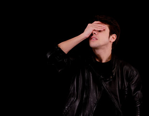 Muscular handsome young man holding his head with black jacket in front of black background