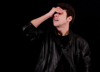 Muscular handsome young man holding his head with black jacket in front of black background.