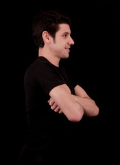 Muscular handsome young man smiling with black tee shirt in front of black background