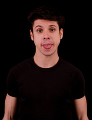 Muscular handsome young man pulling his tongue out with black tee shirt in front of black background