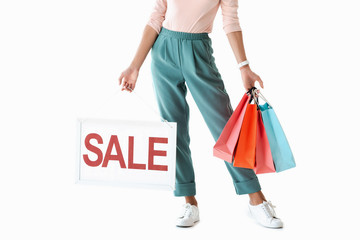 cropped view of beautiful girl holding board with sale sign and shopping bags, isolated on white
