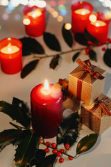 Christmas and New Year composition. Lit candles, present boxes and branch of holly