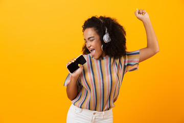 Woman posing isolated over yellow background listening music with headphones dancing singing.