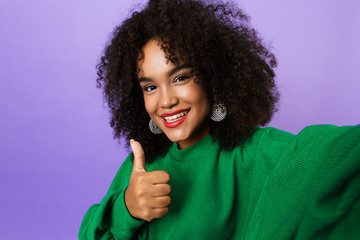 African woman isolated over violet background showing thumbs up gesture take selfie by camera.