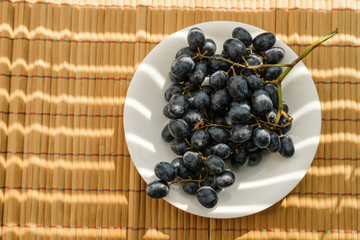 Dark grapes in plate on wooden background.