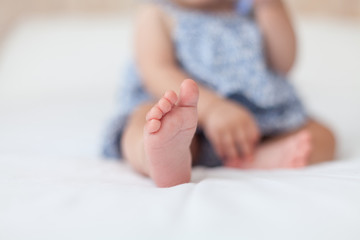 Baby girl small nude foot. Baby sitting on the bed