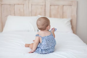 Baby sits back on the bed. Wooden headboard © Анна В
