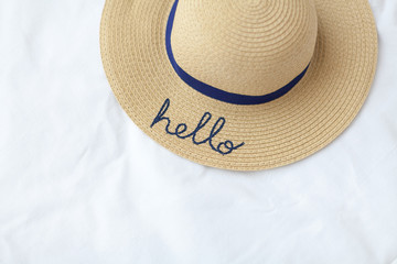 Wicker hat on white textured background. Hello inscription