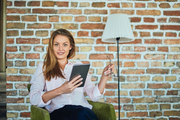 Businesswoman sitting in armchair and using tablet. Next to her lamp.