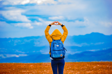 Girl making heart-shape symbol in hilly landscape.