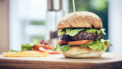 A beef burger in a crusty bun with lettuce and tomatoes on a cho