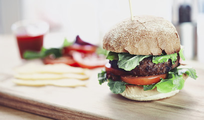 A beef burger in a crusty bun with lettuce and tomatoes on a cho
