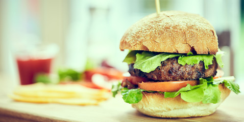 A beef burger in a crusty bun with lettuce and tomatoes on a cho