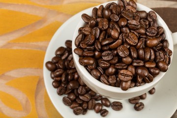 Coffee cup and saucer filled with coffee beans on decorative