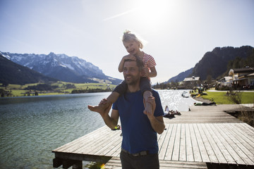 Austria, Tyrol, Walchsee, happy father carrying daughter on shoulders at the lake