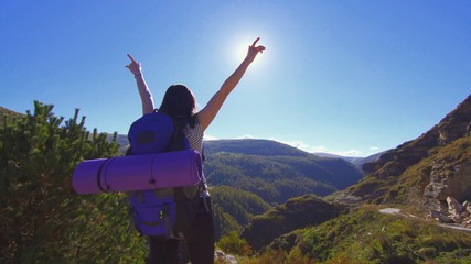 girl tourist with backpack raised his hands up standing on a rock in the mountains