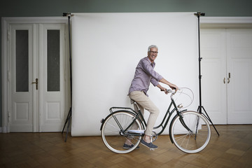 Portrait of mature man posing on bicycle at projection screen