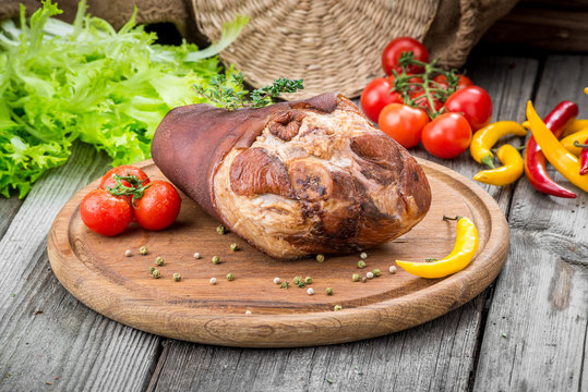 Smoked ham hock with herbs and spices on wooden plate.