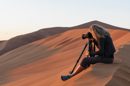 Africa, Namibia, Namib desert, Naukluft National Park, female photographer photographing at early morning light, sitting on sand dune