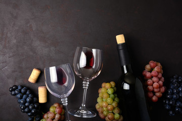 Wineglasses with red wine, bottle, grapes and corks lying on dark wooden background. Top view. Flat lay. Copy space