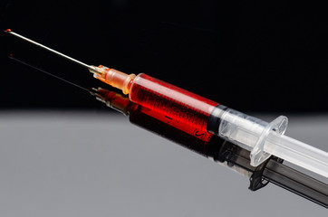 syringe filled with a red liquid on a black acrylic background